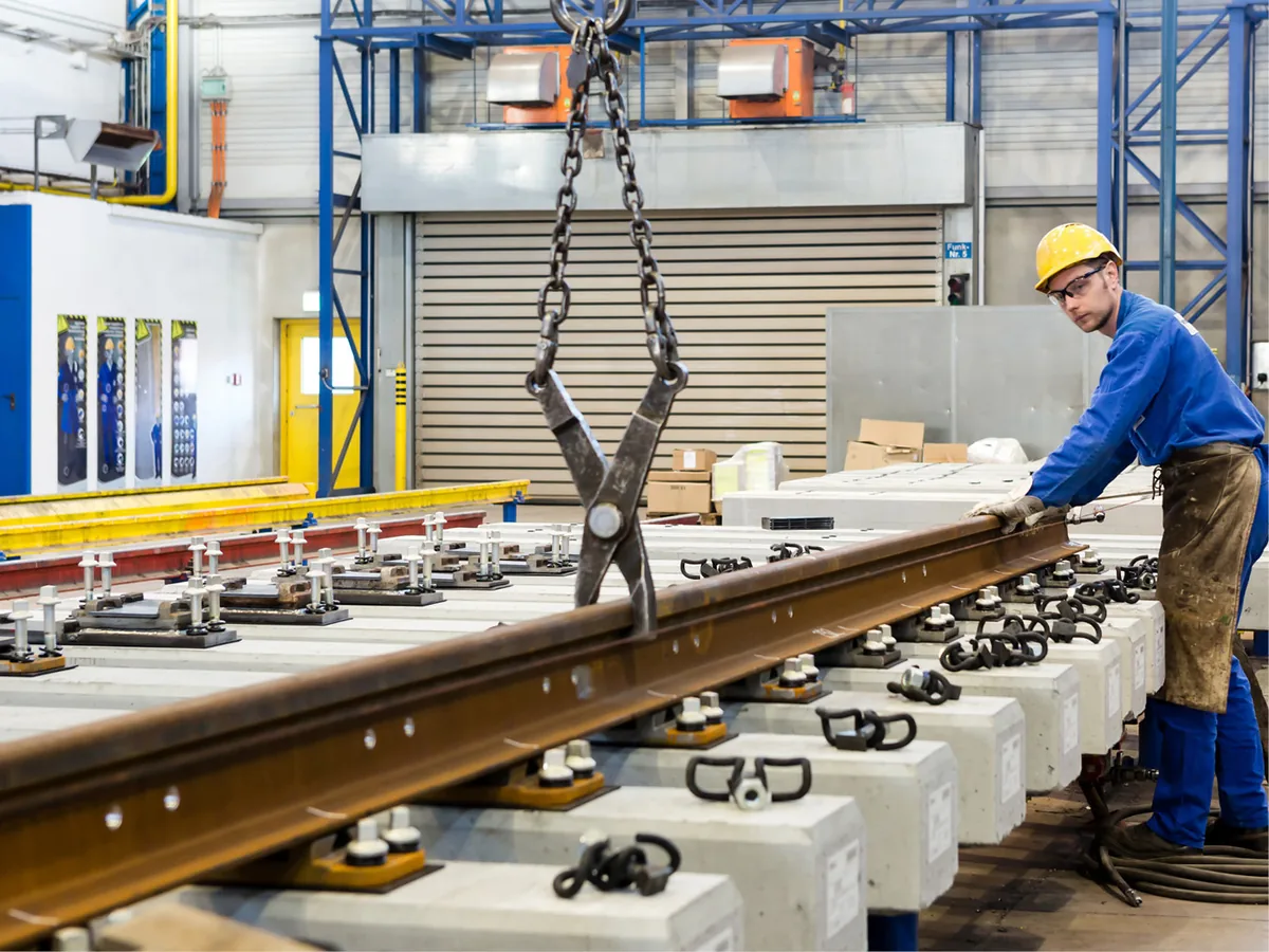 Worker handling rail components in a voestalpine turnout production facility
