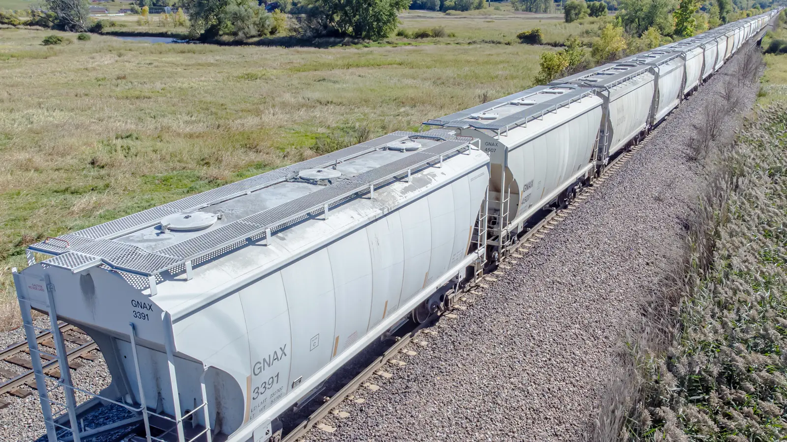 Covered hopper railcars travelling through a rural landscape Covered hopper railcars travelling through a rural landscape