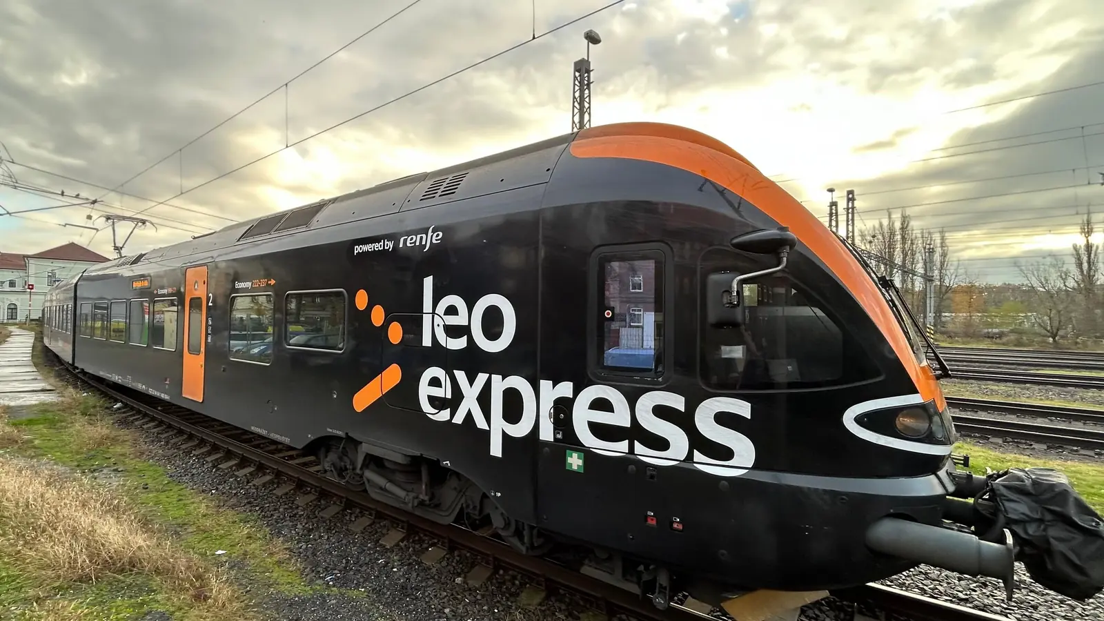 Black-and-orange Leo Express train standing on an electrified railway track.