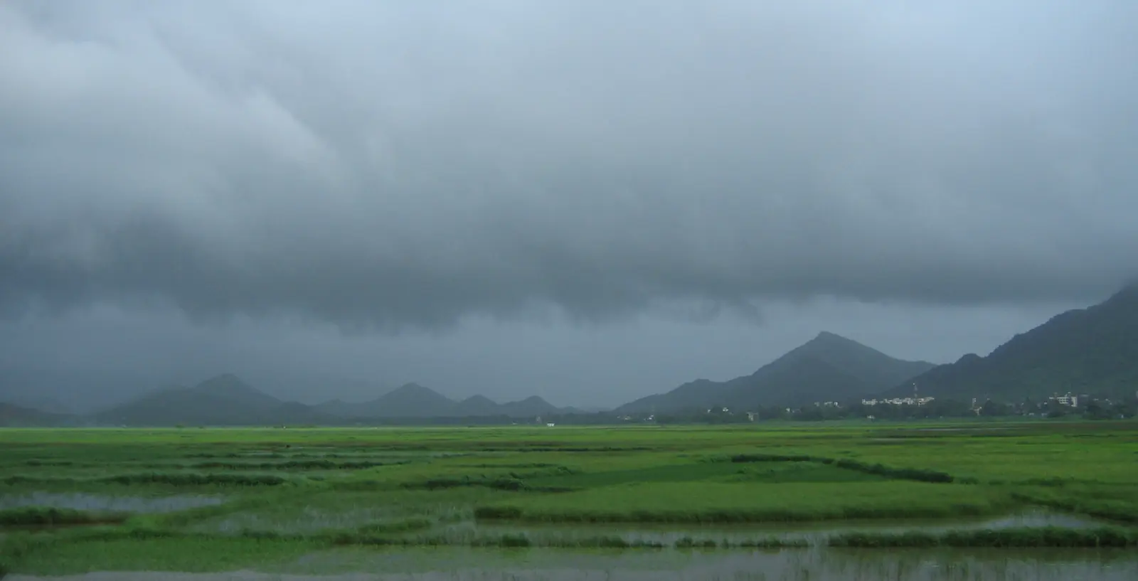Dark monsoon clouds over rain-soaked fields viewed during a Western Railway journey in India. Dark monsoon clouds over rain-soaked fields viewed during a Western Railway journey in India.