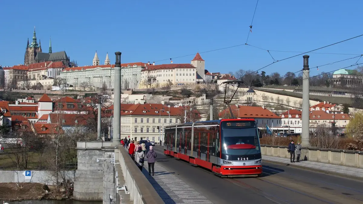 Red Škoda 15T tram crossing a Prague bridge below Prague Castle