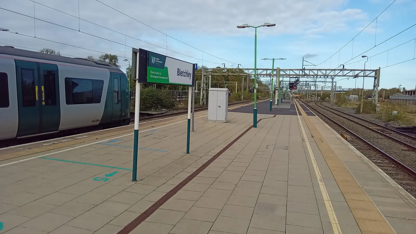 Bletchley station platforms, railway tracks and a train beside the station sign