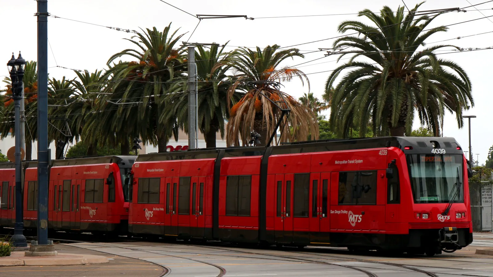 Red San Diego MTS trolley running on street-level tracks beneath overhead wires. Red San Diego MTS trolley running on street-level tracks beneath overhead wires.