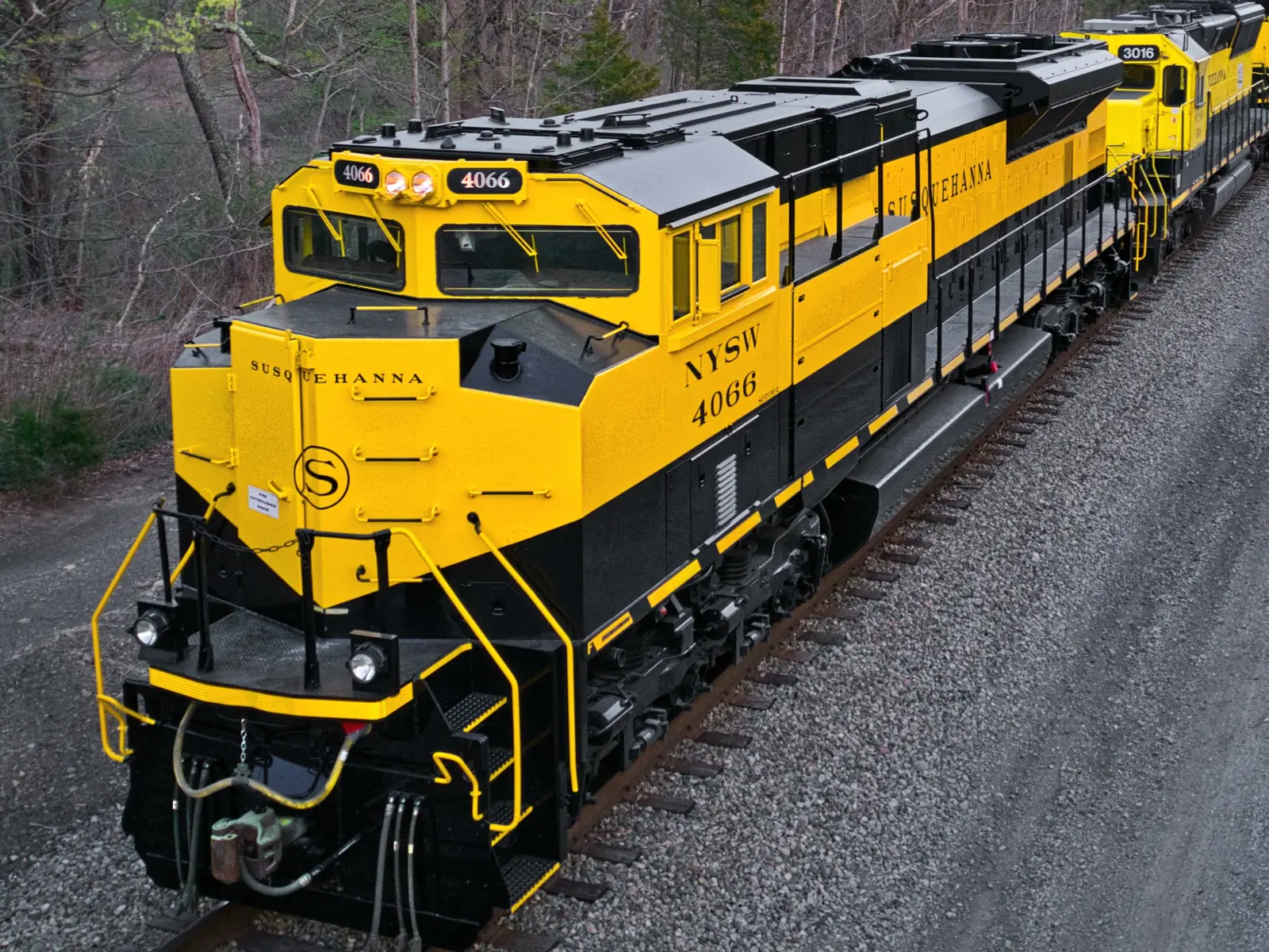Yellow-and-black NYS&W locomotive No. 4066 leading another locomotive through a wooded area. Yellow-and-black NYS&W locomotive No. 4066 leading another locomotive through a wooded area.