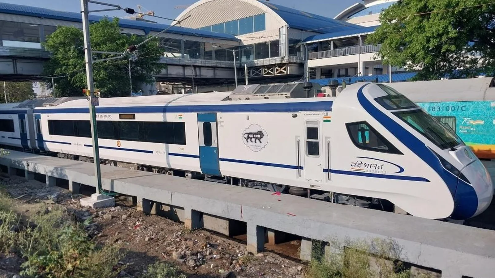 Blue-and-white Vande Bharat trainset standing beside railway infrastructure.