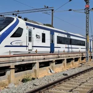 Blue-and-white Vande Bharat Express trainset beside an electrified railway track.