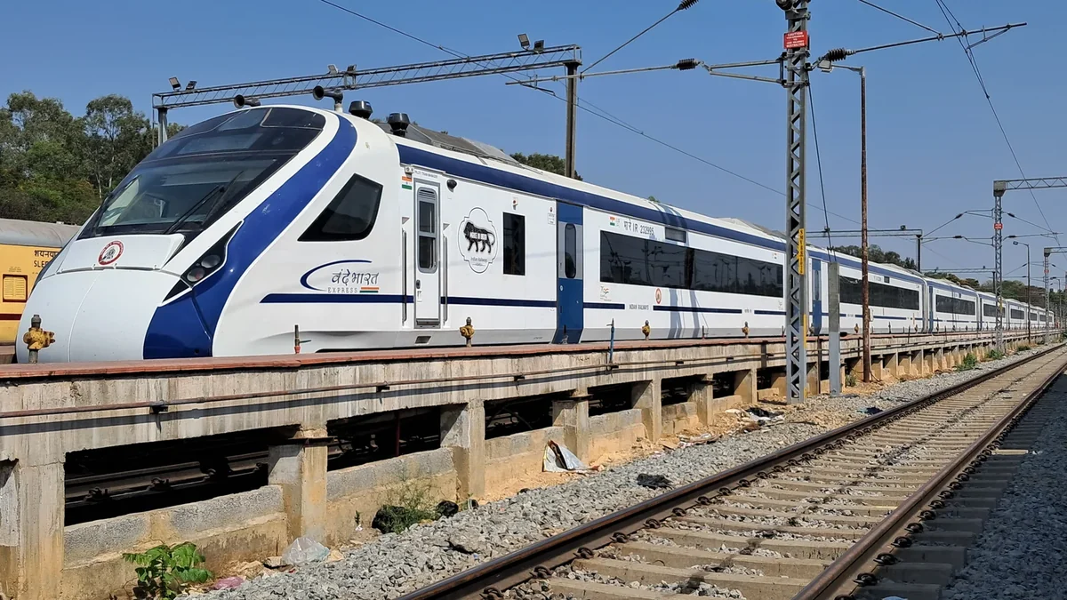 Blue-and-white Vande Bharat Express trainset beside an electrified railway track.