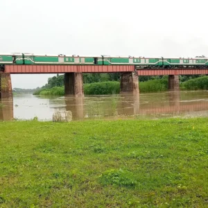 Bangladesh Railway LHB passenger coaches crossing a bridge behind a blue locomotive