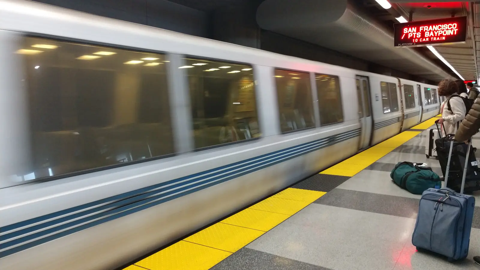 BART riders waiting on a platform as a train arrives at San Francisco International Airport station