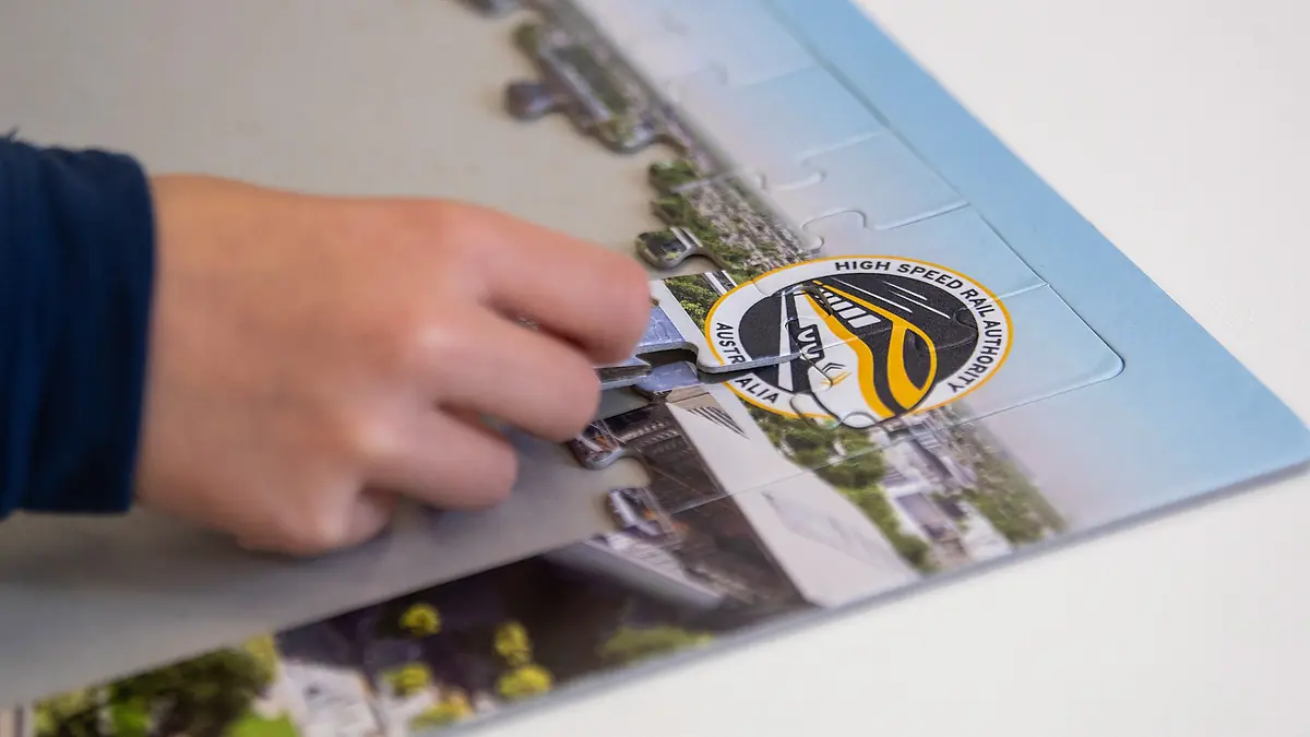 Hand fitting a train piece into a High Speed Rail Authority puzzle