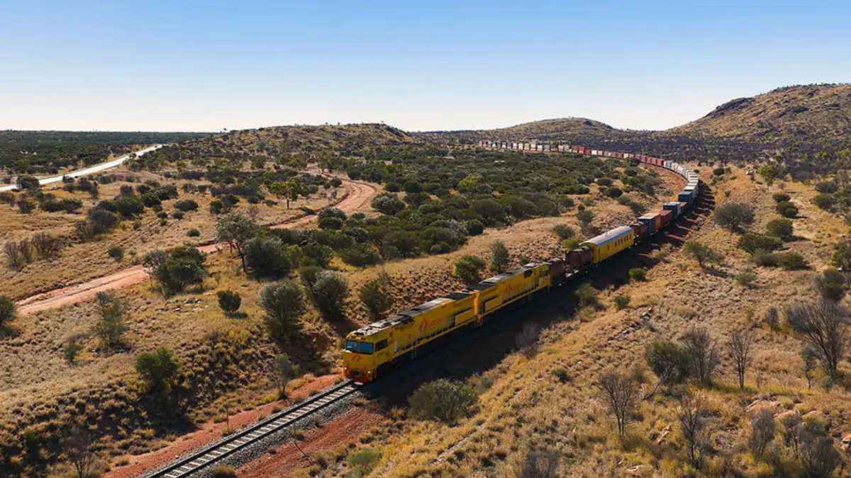 Aurizon double-stack freight train carrying containers through arid terrain near Alice Springs