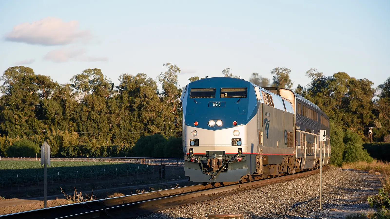 Amtrak locomotive 160 leads a passenger train through a rural rail corridor
