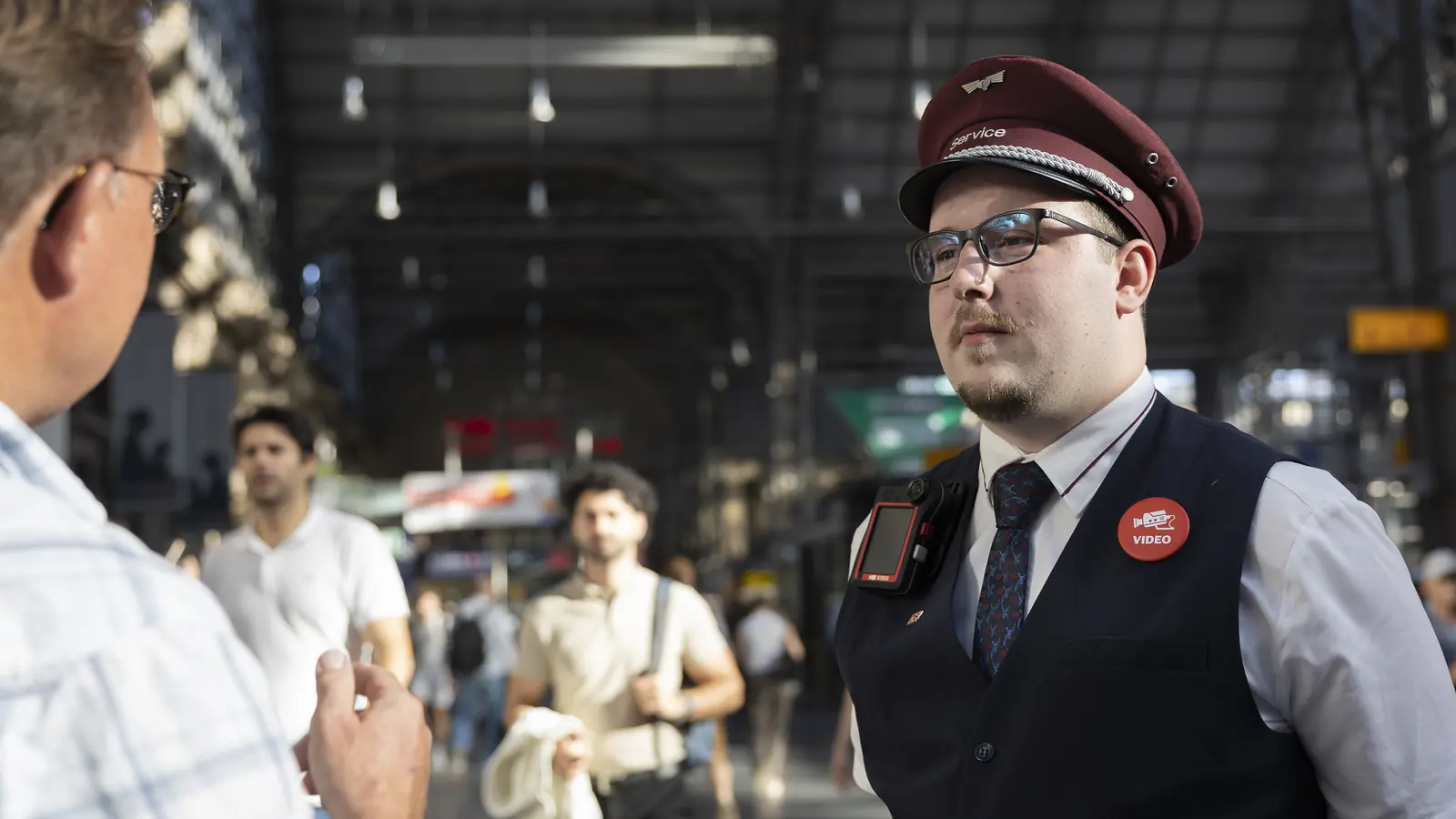 Deutsche Bahn station service employee wearing a bodycam while speaking with a passenger at Frankfurt Central Station