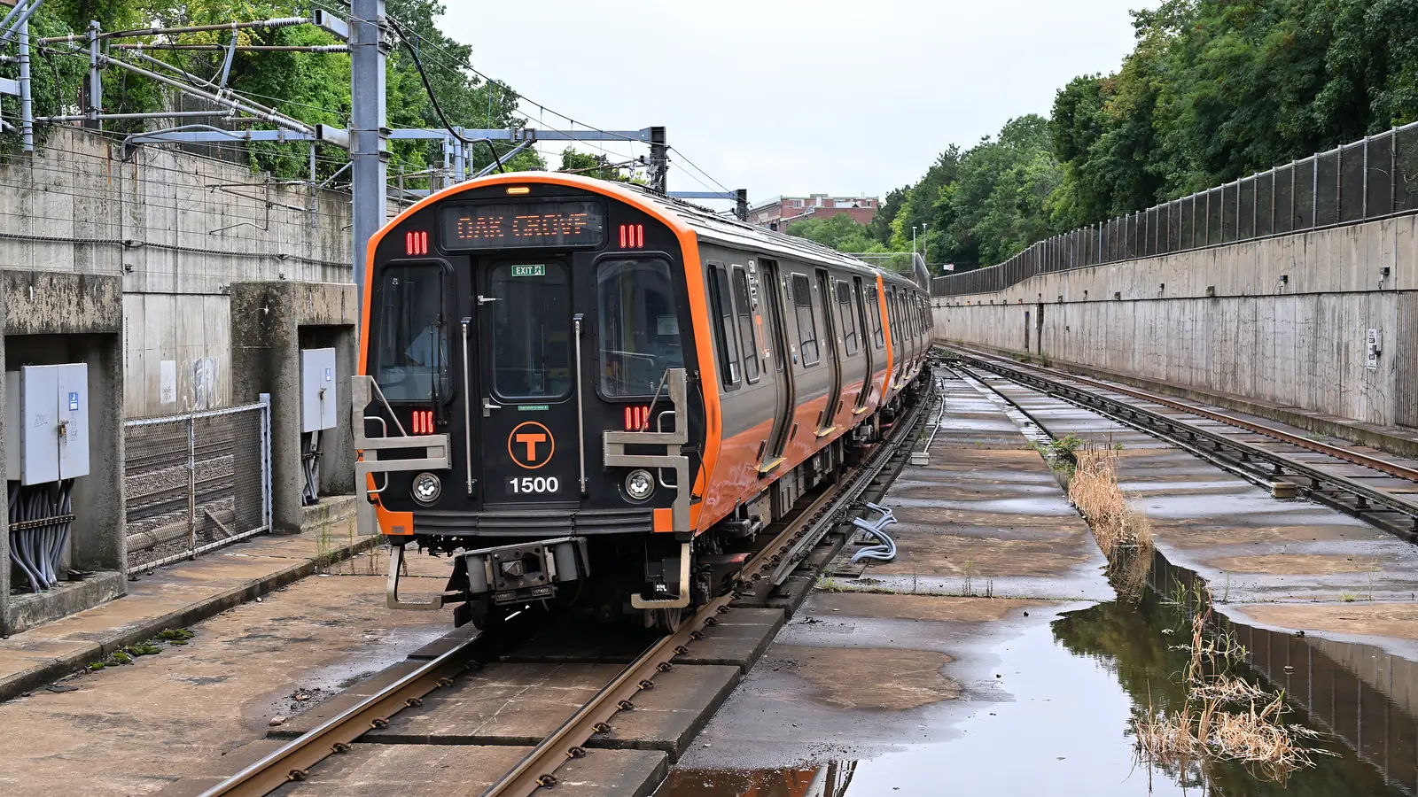 An inbound MBTA Orange Line train approaching Roxbury Crossing on wet tracks.