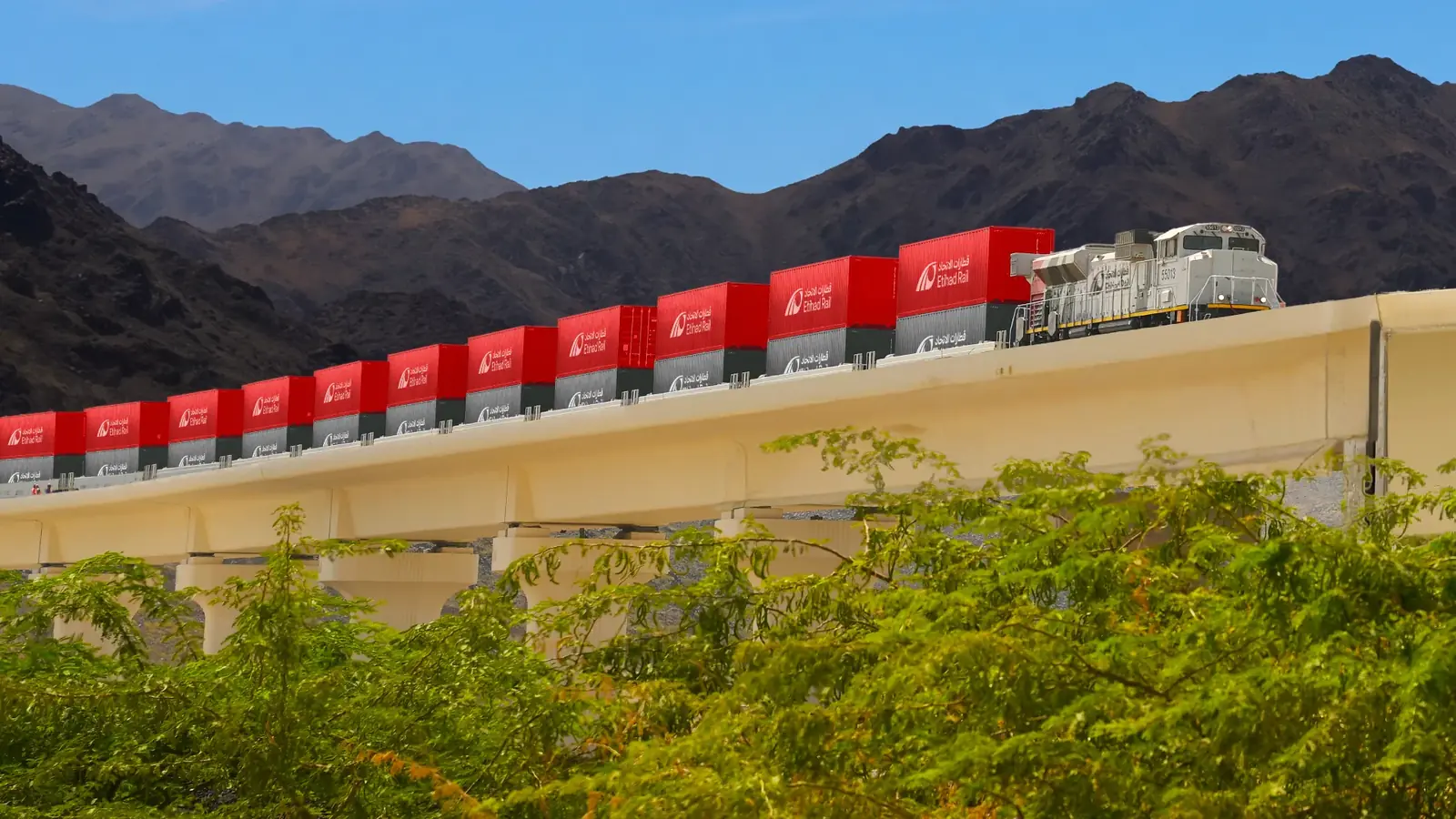 Etihad Rail locomotive hauling double-stacked containers through mountainous terrain