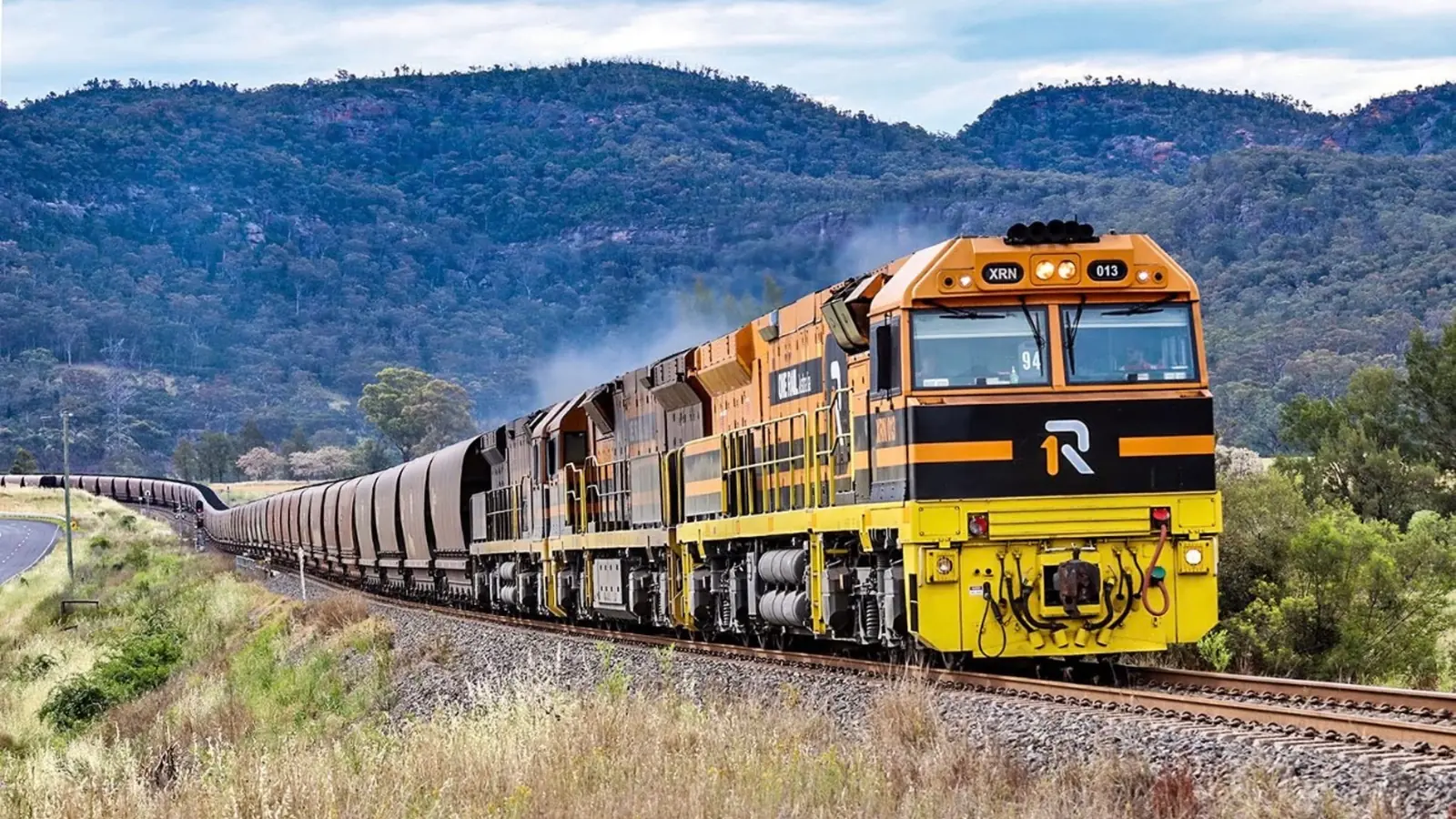 One Rail Australia XRN013 locomotive hauling a freight train through a mountain valley