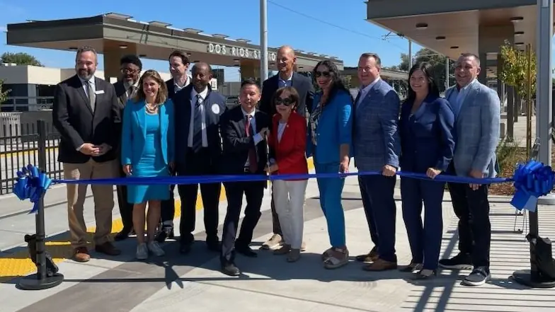 Officials gathered behind a blue ribbon at the completed Dos Rios light rail station