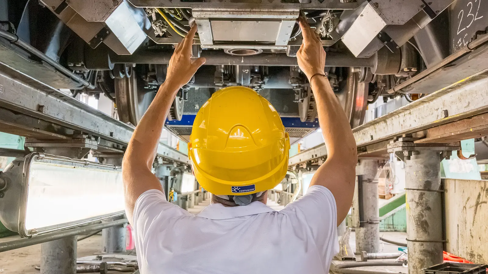 Technician installs a Plasser InertialGeometry unit beneath a railway vehicle