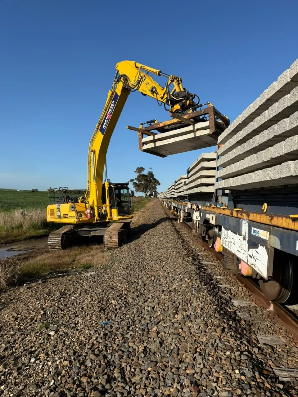 Excavator unloading concrete sleepers from rail wagons along the Maroona–Portland corridor