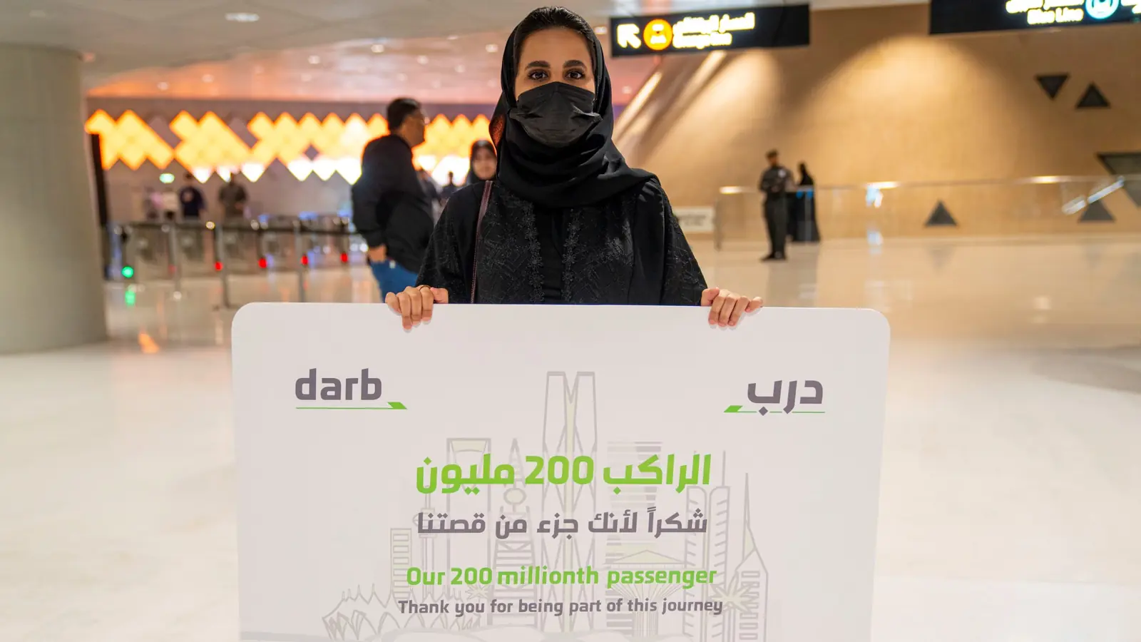 Woman holds a sign marking Riyadh Metro’s 200 millionth passenger inside a station
